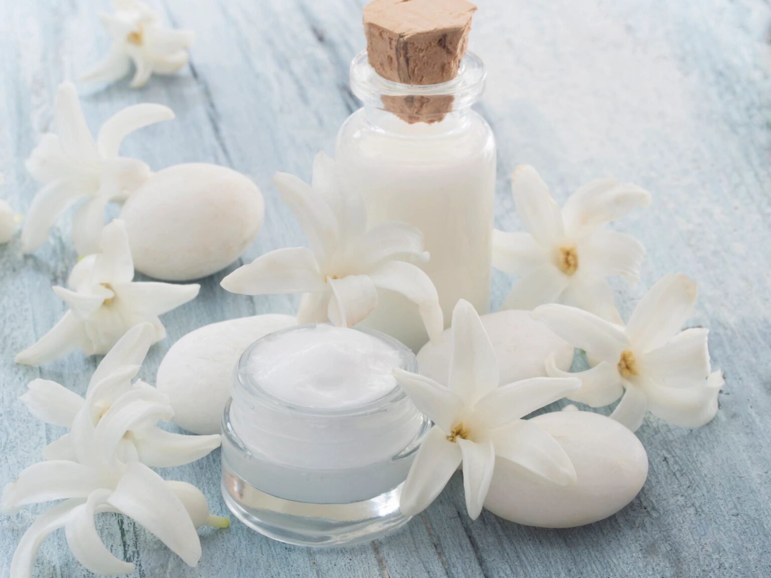 A jar of cream and some white flowers on a table.