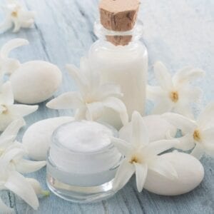 A jar of cream and some white flowers on a table.