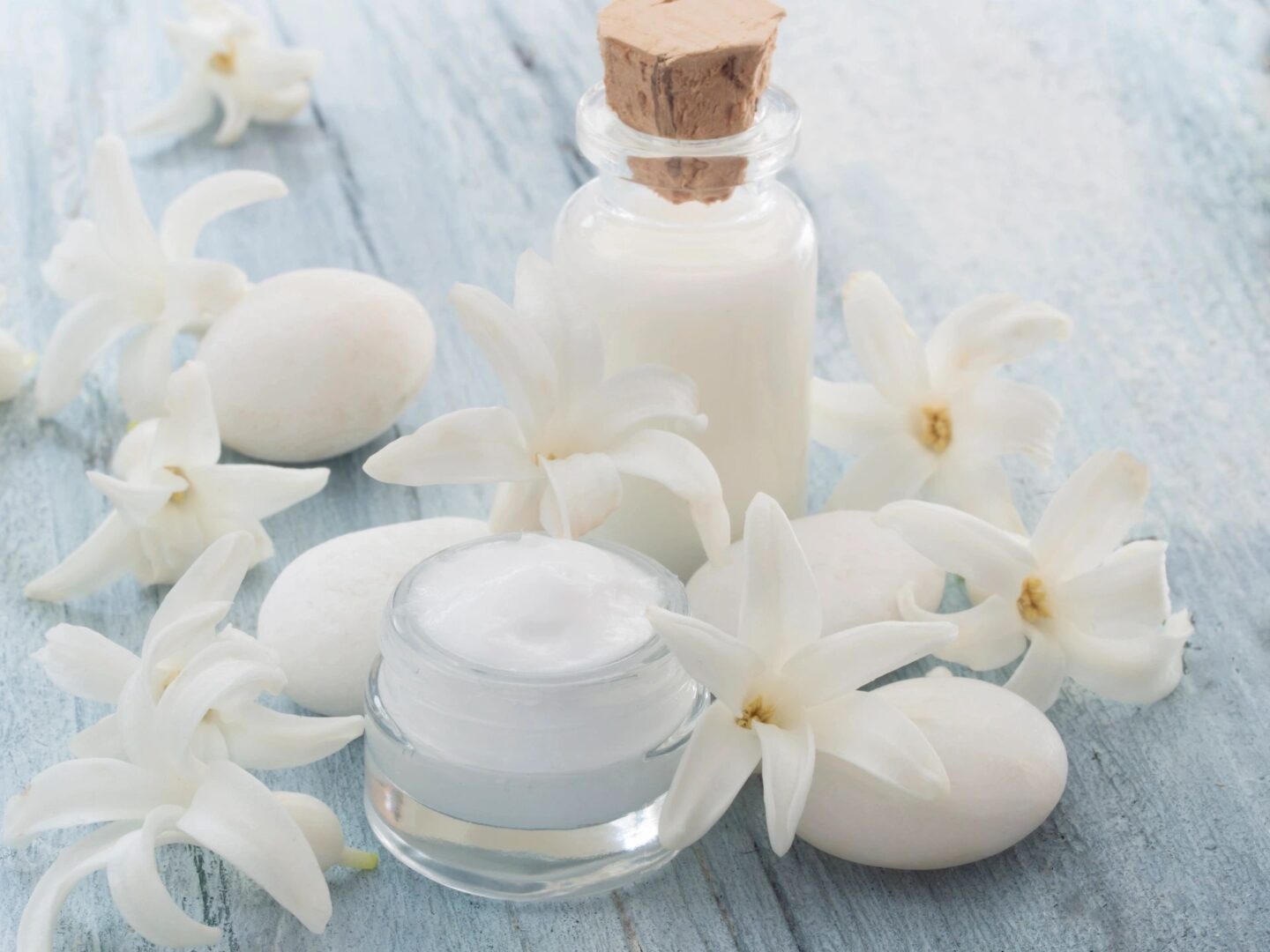 A jar of cream and some white flowers on a table.