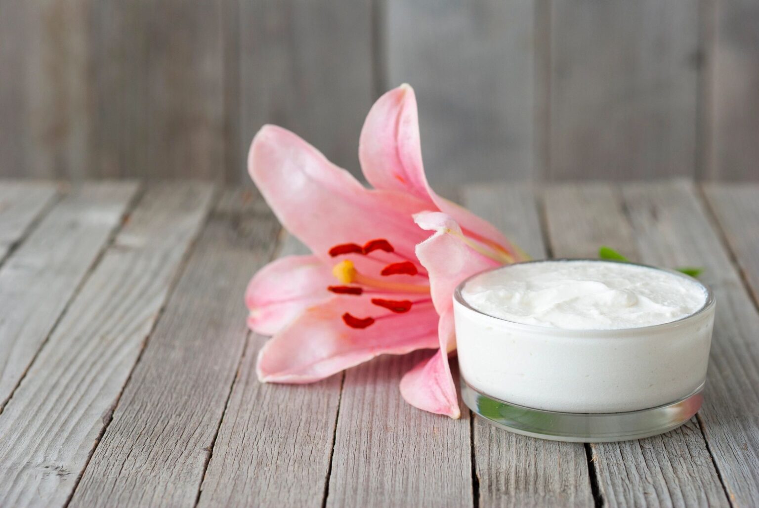 A pink flower and some cream on top of a table.