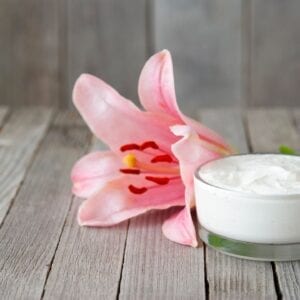 A pink flower and some cream on top of a table.